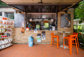 Buitencafé op Camping Colleverde in Toscane, Italië, met snacks, menuborden en oranje stoelen.