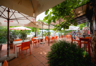 Buitencafé met oranje stoelen, parasols en groene planten op Camping Colleverde, Toscane, Italië.