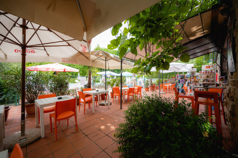 Buitencafé met oranje stoelen, parasols en groene planten op Camping Colleverde, Toscane, Italië.
