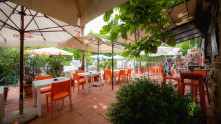 Zona de cafetería al aire libre con sillas naranjas, sombrillas y plantas en Camping Colleverde, Toscana.