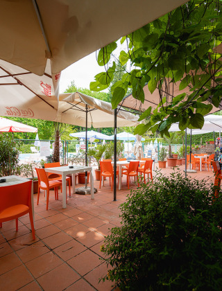 Außenterrasse mit orangefarbenen Stühlen, Sonnenschirmen und viel Grün im Camping Colleverde, Toskana.