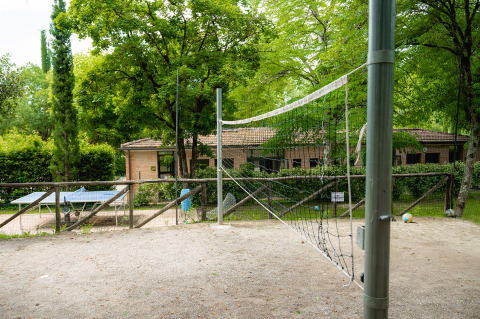 Cancha de voleibol exterior y mesa de ping-pong en Camping Colleverde, Toscana, Italia, rodeados de árboles.