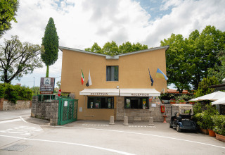 Receptie bij Camping Colleverde in Toscane, Italië, met vlaggen, bomen en een golfkar buiten.