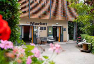Ingresso del market al Camping Colleverde in Toscana, Italia, con fiori colorati in primo piano.