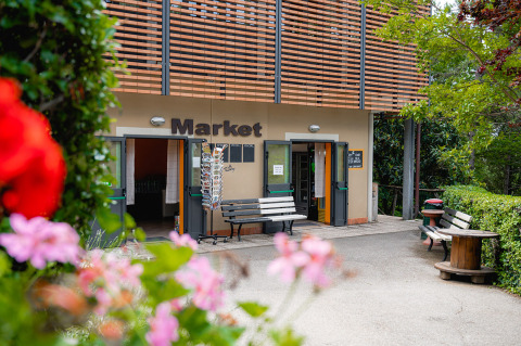 Entrée du marché du Camping Colleverde en Toscane, Italie, avec des fleurs colorées au premier plan.