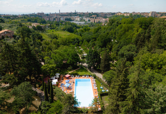 Luchtfoto van het zwembad op Camping Colleverde, tussen bomen met zicht op Siena in het Toscaanse landschap.