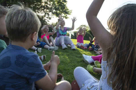 Niños sentados en círculo juegan sobre el césped en Camping de Molenhoek, un parque vacacional en Zeeland.