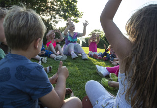 Børn sidder i en cirkel på græsset og leger udendørs ved Camping de Molenhoek i Zeeland, Holland.