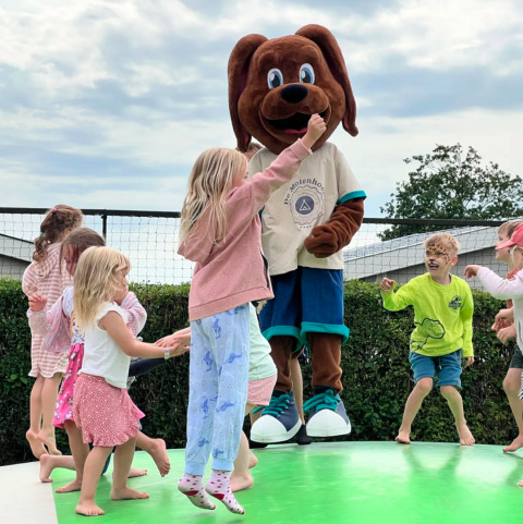 Kinder spielen und springen mit einem Hundemaskottchen auf einem Spielplatz im Camping de Molenhoek, Zeeland.