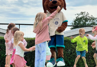 Kinder spielen und springen mit einem Hundemaskottchen auf einem Spielplatz im Camping de Molenhoek, Zeeland.