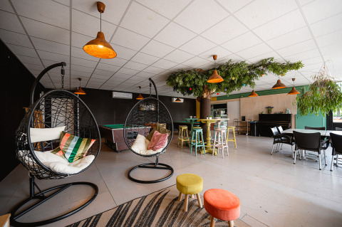 Area lounge moderna con sedie sospese, sgabelli colorati e piante al Camping de Molenhoek nei Paesi Bassi.