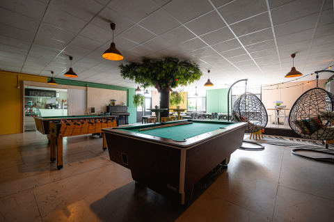 Sala de recreo en Camping de Molenhoek con mesa de billar, futbolín y sillas colgantes para relajarse.