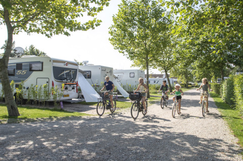 Famiglie in bicicletta lungo un vialetto accanto a roulotte al Camping de Molenhoek, parco vacanze in Zeeland, Olanda.