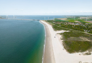 Vista aerea di spiaggia, mare e Camping de Molenhoek con pale eoliche a Zeeland, Paesi Bassi, giornata limpida.