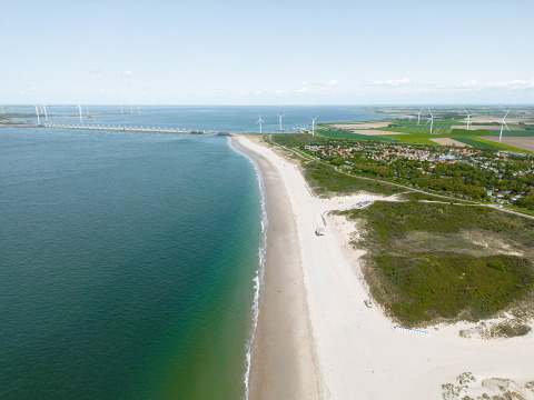 Luftaufnahme eines Strandes mit Windrädern und Ferienpark in Zeeland, Niederlande, bei Camping de Molenhoek.