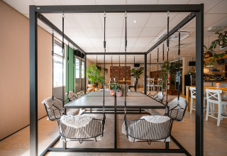 Spazio moderno con sedie altalena attorno a un tavolo, piante verdi e arredo accogliente.