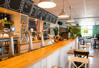 Zona bar luminosa e moderna con spillatori di birra presso Camping de Molenhoek, parco vacanze in Zelanda.
