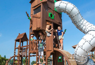 Kinderen spelen op een grote speeltuin met toren en glijbaan bij Camping de Molenhoek, Zeeland, Nederland.