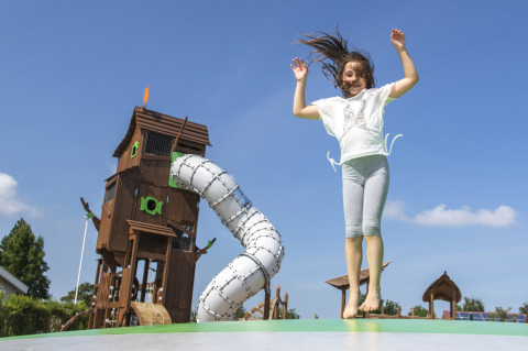 Ragazza che salta su un cuscino elastico davanti a un grande parco giochi a Camping de Molenhoek, Zelanda, Paesi Bassi.