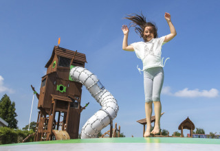 Ragazza che salta su un cuscino elastico davanti a un grande parco giochi a Camping de Molenhoek, Zelanda, Paesi Bassi.