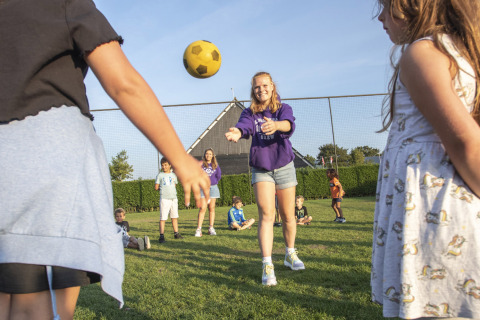 Kinderen spelen met een gele bal op het gras bij Camping de Molenhoek, een vakantiepark in Zeeland, Nederland.