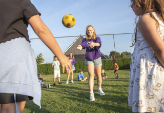 Children are playing with a yellow ball on the grass at Camping de Molenhoek holiday park in Zeeland, Netherlands.