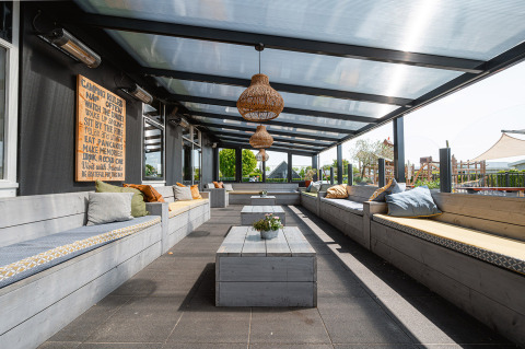Covered outdoor lounge with cushioned wooden benches at Camping de Molenhoek holiday park in Zeeland.