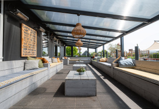 Covered outdoor lounge with cushioned wooden benches at Camping de Molenhoek holiday park in Zeeland.