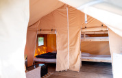 Interieur van Safari tent met houten vloer, stapelbedden en knusse slaapruimte, raam met zonlicht.