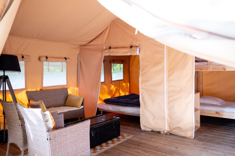 Intérieur d'une tente safari avec coin salon confortable, lit double, lits superposés et sol en bois