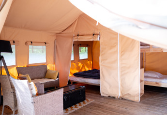 Interior of a safari tent featuring cozy seating, a double bed, bunk beds, and wooden flooring