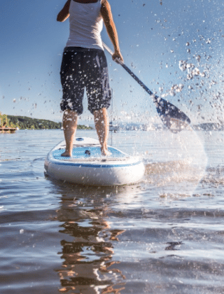 Persona haciendo paddle surf en un lago en un parque vacacional con alojamientos tipo glamping.