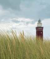 Un faro rojo se eleva entre la hierba de playa bajo un cielo nublado cerca de Sommelsdijk, Holanda Meridional.