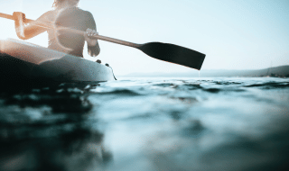 Persona navegando en kayak en un lago en un parque vacacional con alojamiento glamping al amanecer.