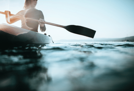 Personne faisant du kayak sur un lac dans un parc de vacances proposant du glamping, à la lumière du matin.
