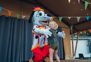 Barn krammer en dalmatiner-maskot på scenen under festlige flag ved Camping de Papillon, Overijssel.