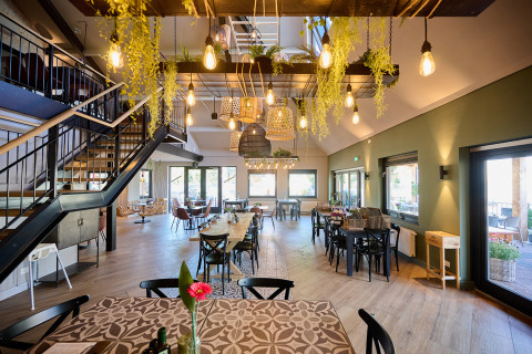 Interior de restaurante luminoso con luces colgantes y plantas en Camping de Papillon, Overijssel, Países Bajos.