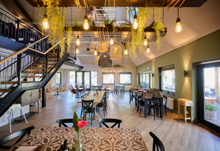 Modern restaurant met hanglampen en veel groen in Camping de Papillon, Overijssel, Nederland.
