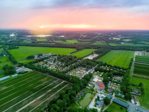 Vista aérea del parque de vacaciones Camping de Papillon en Overijssel, Países Bajos, rodeado de campos al atardecer.