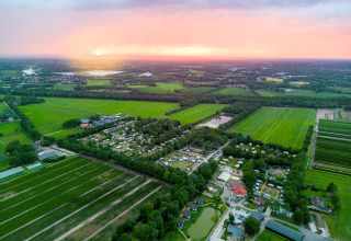 Luchtfoto van het Camping de Papillon vakantiepark in Overijssel, Nederland, omgeven door groene velden bij zonsondergang.