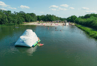Luchtfoto van een zwemvijver, strand en opblaasbaar speeltoestel op Camping de Papillon, Overijssel, Nederland.