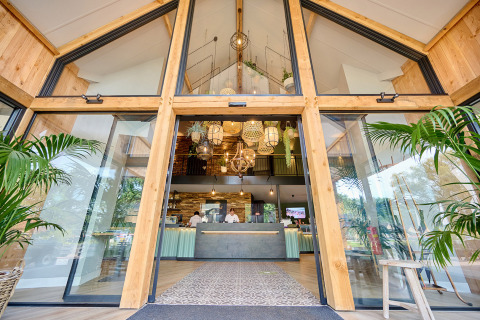 Entrada al Camping de Papillon, parque vacacional en Overijssel, Países Bajos, con puertas de cristal y plantas.