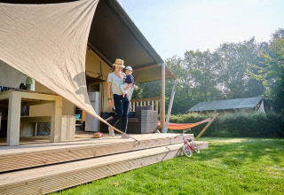 Moeder met kind op houten terras bij tent op Camping de Papillon, Overijssel, Nederland, zonnige dag.