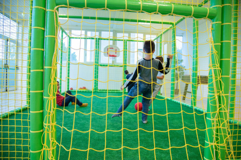 Niños juegan fútbol en una zona de juegos interior con redes verdes y amarillas en Camping de Papillon, Overijssel.