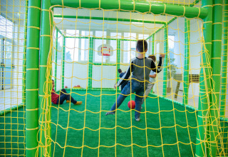 Kinderen spelen voetbal in een indoor speelruimte met groene en gele netten bij Camping de Papillon, Overijssel.