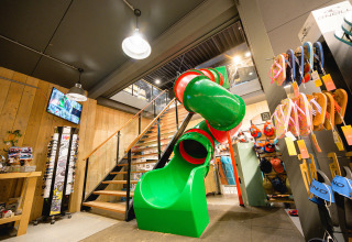 Groene glijbaan en trap in een winkel op Camping de Schatberg vakantiedomein in Limburg, Nederland.