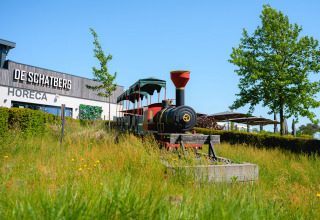 A colorful toy train stands in front of De Schatberg holiday park in Limburg, Netherlands, on a sunny day.