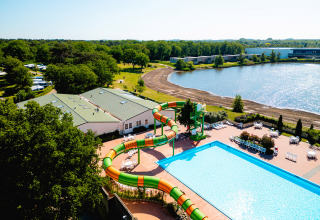 Luftfoto af Camping de Schatberg i Limburg, Holland med pool, vandrutsjebane og sø i sommersol.