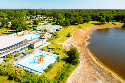 Veduta aerea di Camping de Schatberg in Limburgo, con piscine, scivoli d'acqua e spiaggia sabbiosa sul lago.