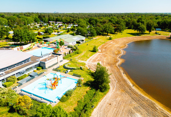 Aerial view of Camping de Schatberg holiday park in Limburg, with pools, waterslides and a sandy lakeshore.